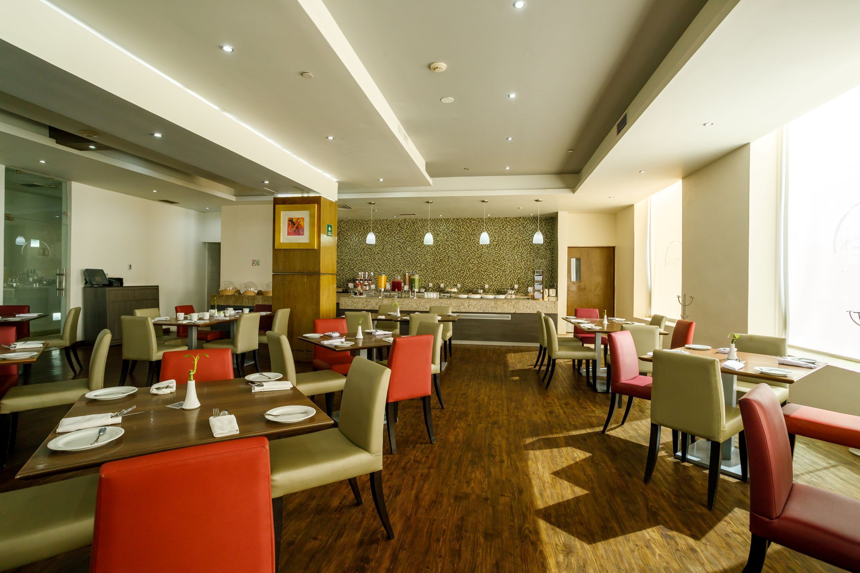 A modern restaurant with multiple dining tables and chairs, a kitchen area, and a bar.