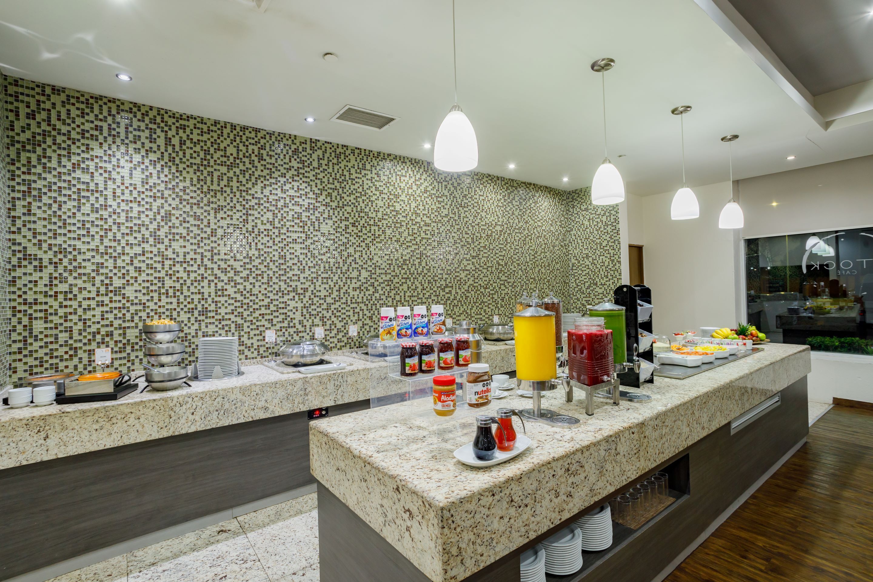 A buffet area with a variety of food items and condiments, a tiled backsplash, and pendant lighting.