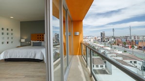 A hotel room with a balcony, a bed, and a city view.