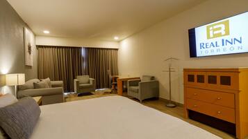 Une chambre d’hôtel avec un grand lit, deux fauteuils, un bureau, une commode et un téléviseur affichant le logo de l’hôtel Real Inn Torreón.