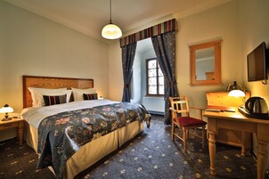 Quarto de hotel com cama, escrivaninha, cadeira, espelho e janela com cortinas.
