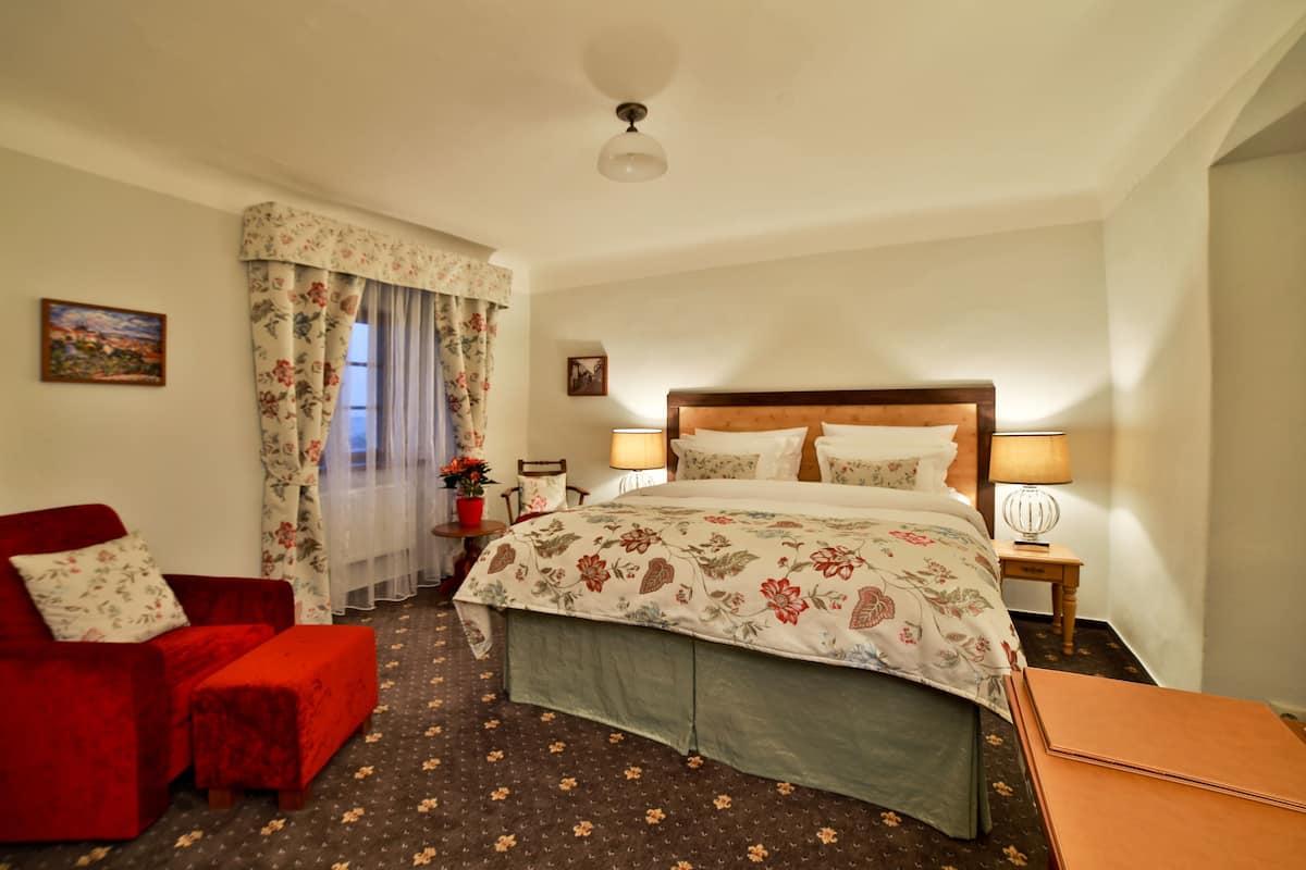 Una habitación de hotel con una cama, un sofá rojo, una mesita con lámpara y una ventana con cortinas.