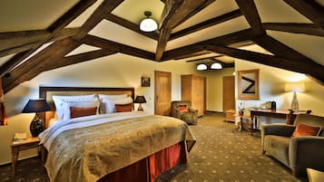 A bedroom with a large bed, wooden beams, a desk, and a chair.