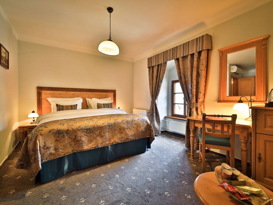 Habitación de hotel con cama, escritorio, silla, espejo y ventana con cortinas.