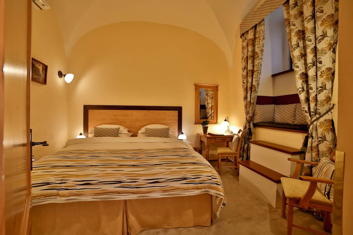 Un dormitorio con una cama grande, un cabecero de madera, un escritorio con una silla y una ventana con cortinas florales.