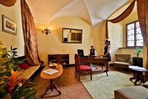 Um quarto acolhedor com sofá, mesa de jantar e escrivaninha com computador. Há uma janela com cortinas, um espelho na parede e uma planta.