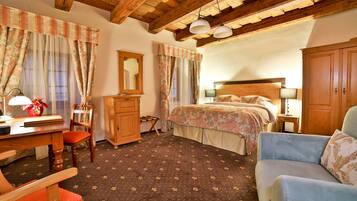 Une chambre avec un plafond en bois, un lit avec une literie à motifs floraux, un bureau avec une lampe, une chaise et une armoire.