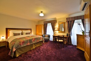 Quarto de hotel com cama, escrivaninha, cadeira, guarda-roupa e espelho.