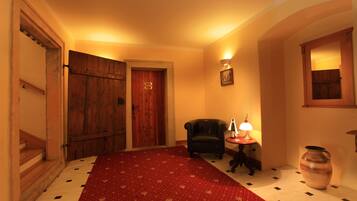 A hallway with a red carpet, wooden doors, a black leather chair, a table with a lamp, and a large vase.