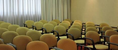 Rows of yellow chairs with black frames arranged in a conference room with a red carpet and a large window with vertical blinds.