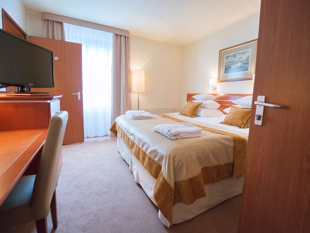 A hotel room with a bed, a desk, a television, and a painting on the wall.