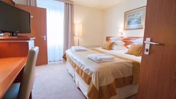 A hotel room with a bed, a desk, a television, and a painting on the wall.