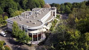 Um edifício moderno com telhado plano, cercado por vegetação exuberante e vista para o mar.