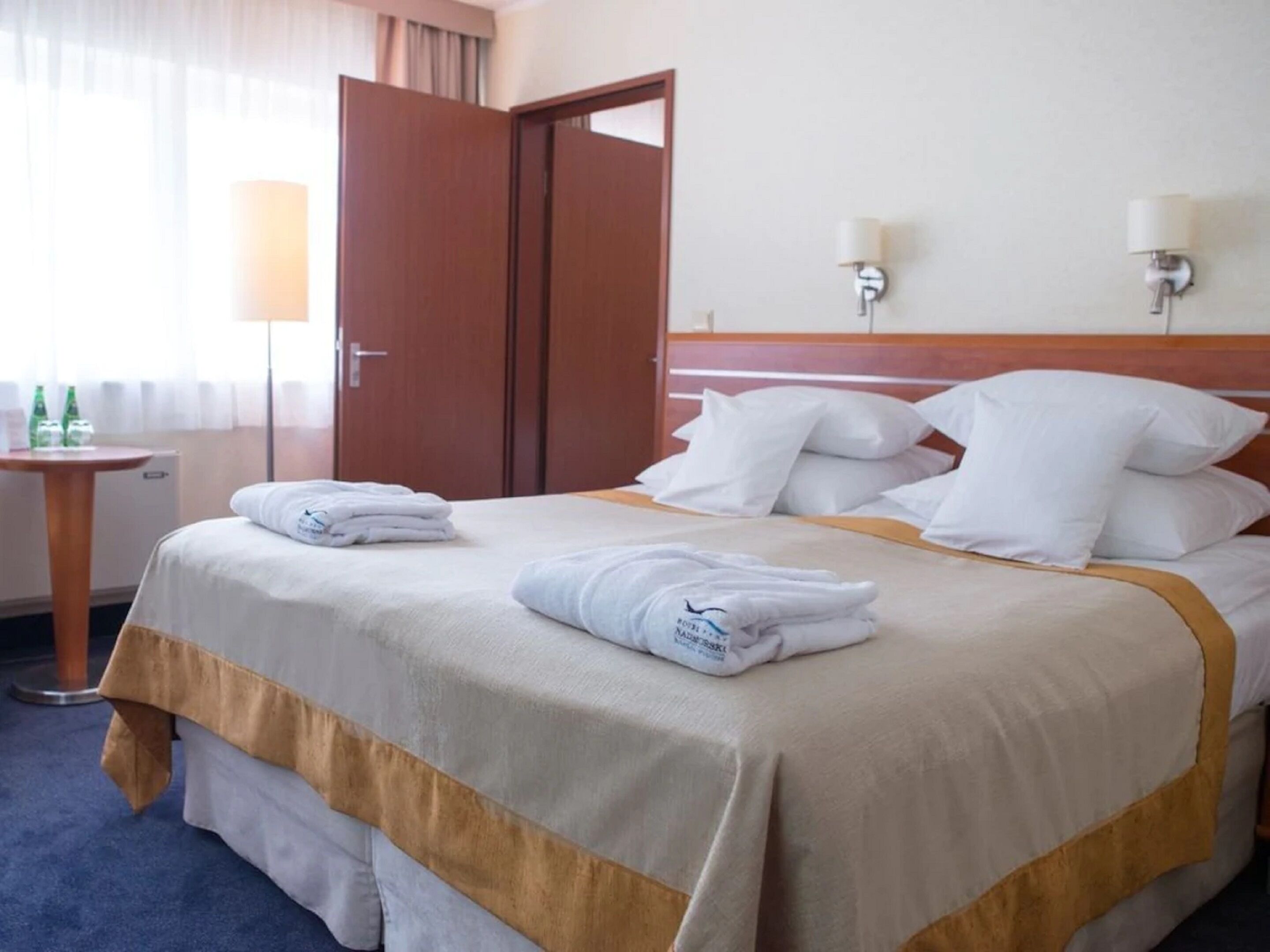 A hotel room with a neatly made bed, two bedside lamps, a wooden door, and a small table with a lamp.