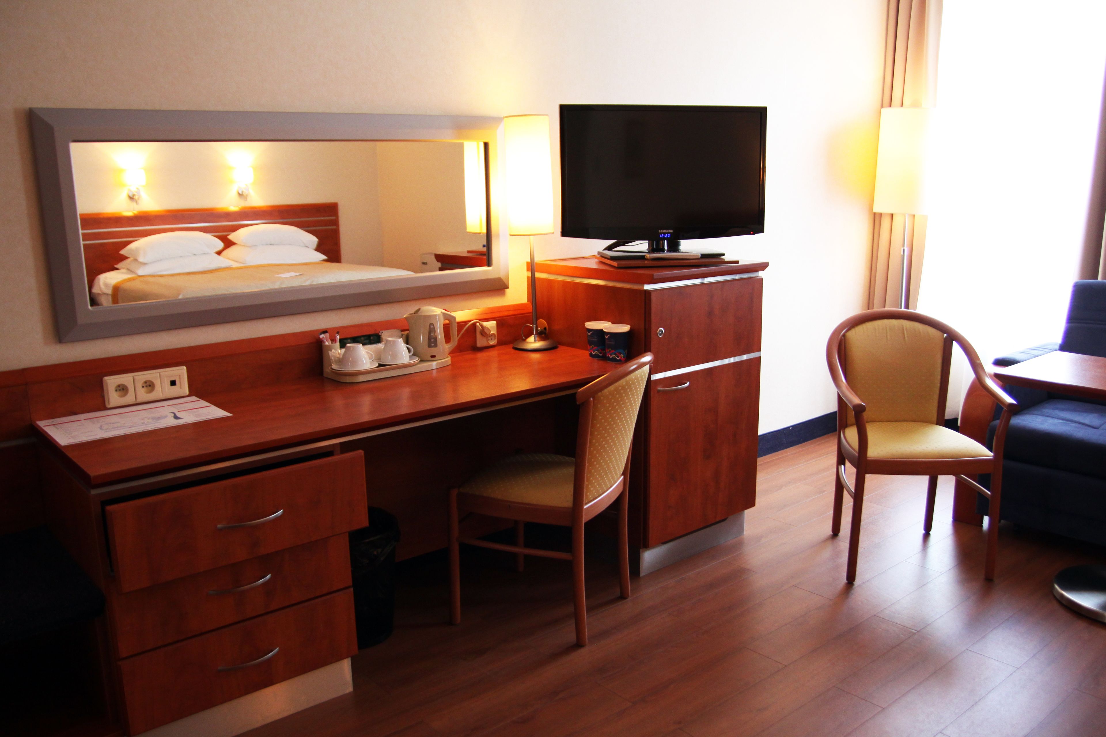 Ein Hotelzimmer mit einem Holztisch, einem Fernseher, einem Sessel und einem Bett mit Kopfteil.