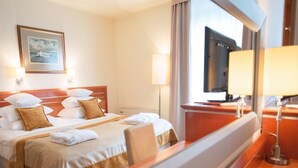 Quarto de hotel com cama, televisão e janela com cortinas.