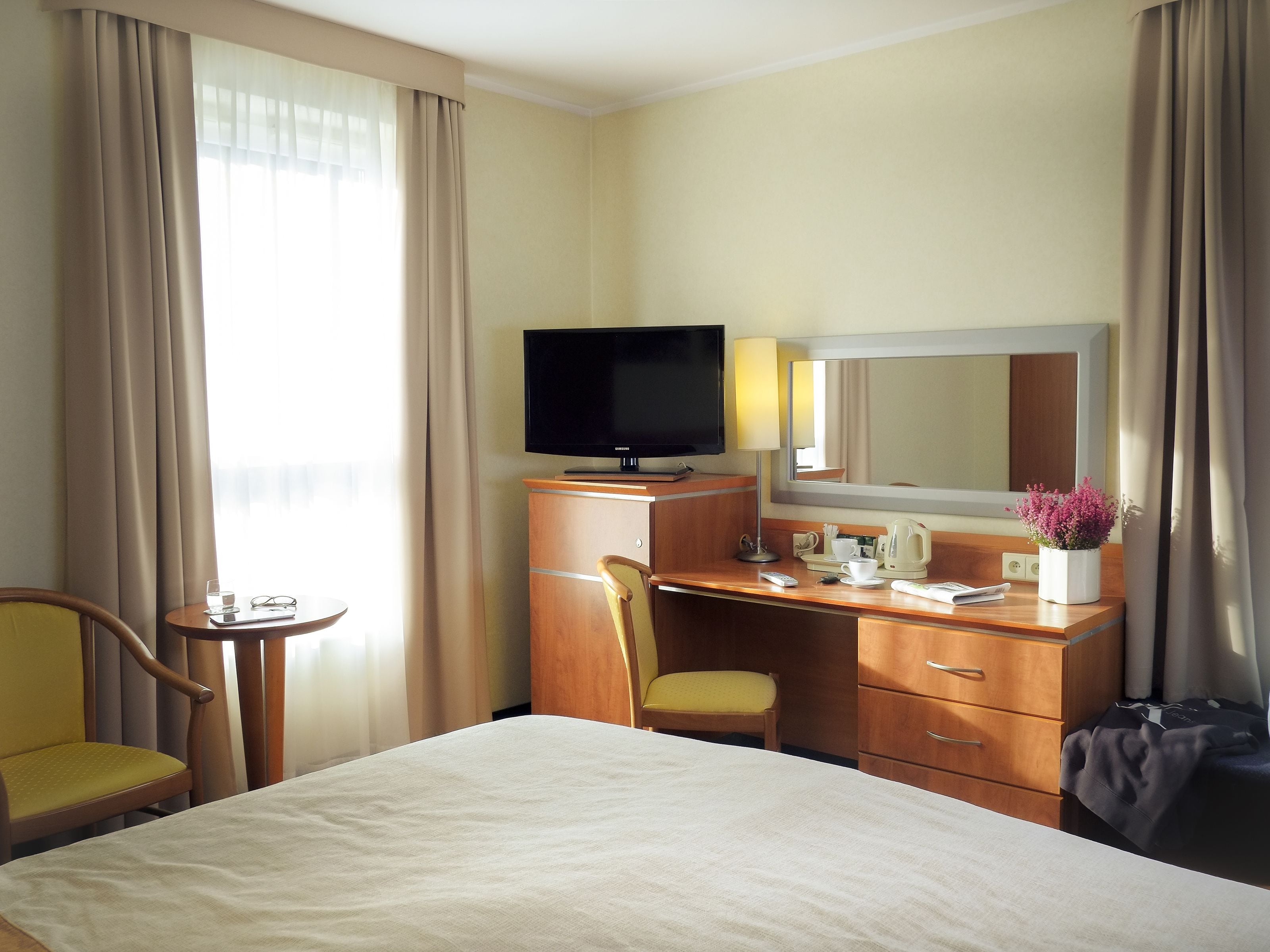 Una habitación de hotel con cama, escritorio con televisor, silla, mesita y espejo.