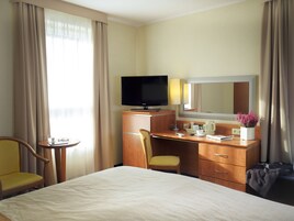Una habitación de hotel con cama, escritorio con televisor, silla, mesita y espejo.