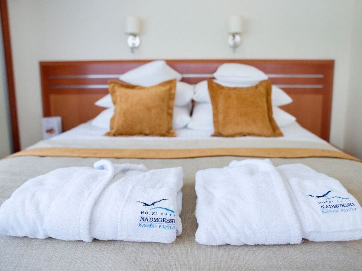 A hotel room with a bed, two pillows, and two towels with the hotel's logo.