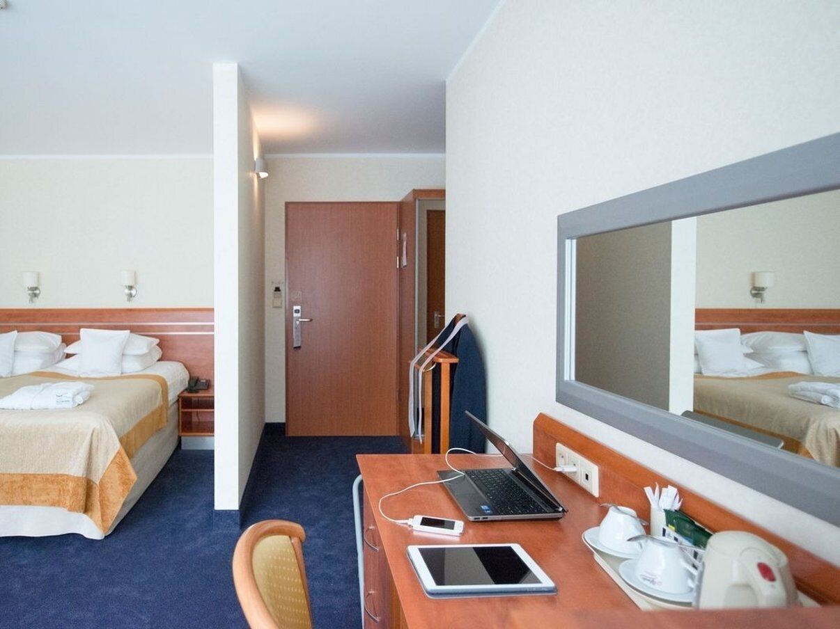 A hotel room with two beds, a desk with a laptop, a tablet, and a mirror.