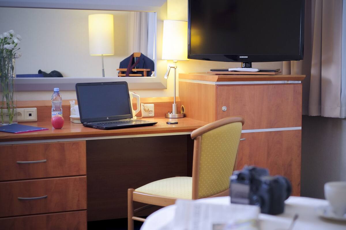 Una habitación de hotel con un escritorio de madera, una computadora portátil, un televisor y una silla.