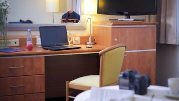 Una habitación de hotel con un escritorio de madera, una computadora portátil, un televisor y una silla.