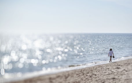 Escena de playa con una persona caminando por la orilla.