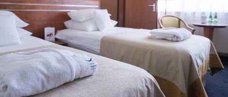 Une chambre d’hôtel avec deux lits, une tête de lit en bois, une table de chevet avec une lampe et une fenêtre avec des rideaux.