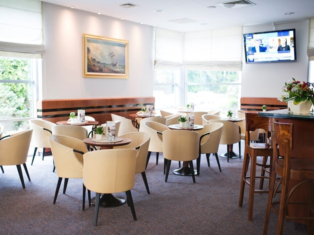 Un comedor de hotel con mesas y sillas redondas, una pantalla de televisión y un cuadro en la pared.