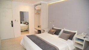 Moderni hotellihuone, jossa on suuri sänky, yöpöydät, vaatekaappi ja peili.