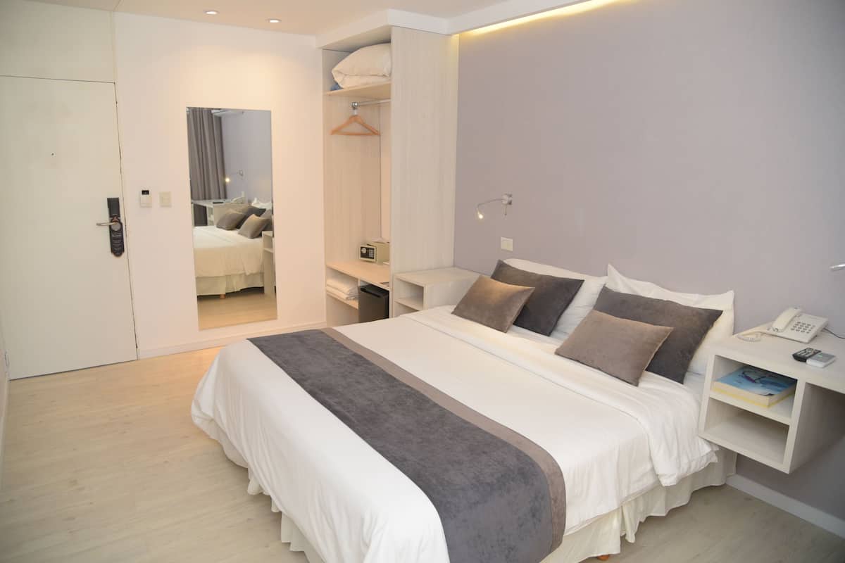 A modern hotel room with a large bed, bedside tables, a wardrobe, and a mirror.