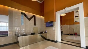 Un área de recepción moderna con un gran logotipo 'M', una pantalla digital y un piso de baldosas limpias.