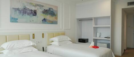 A hotel room with two beds, a painting on the wall, a wardrobe, and a small table with a kettle.