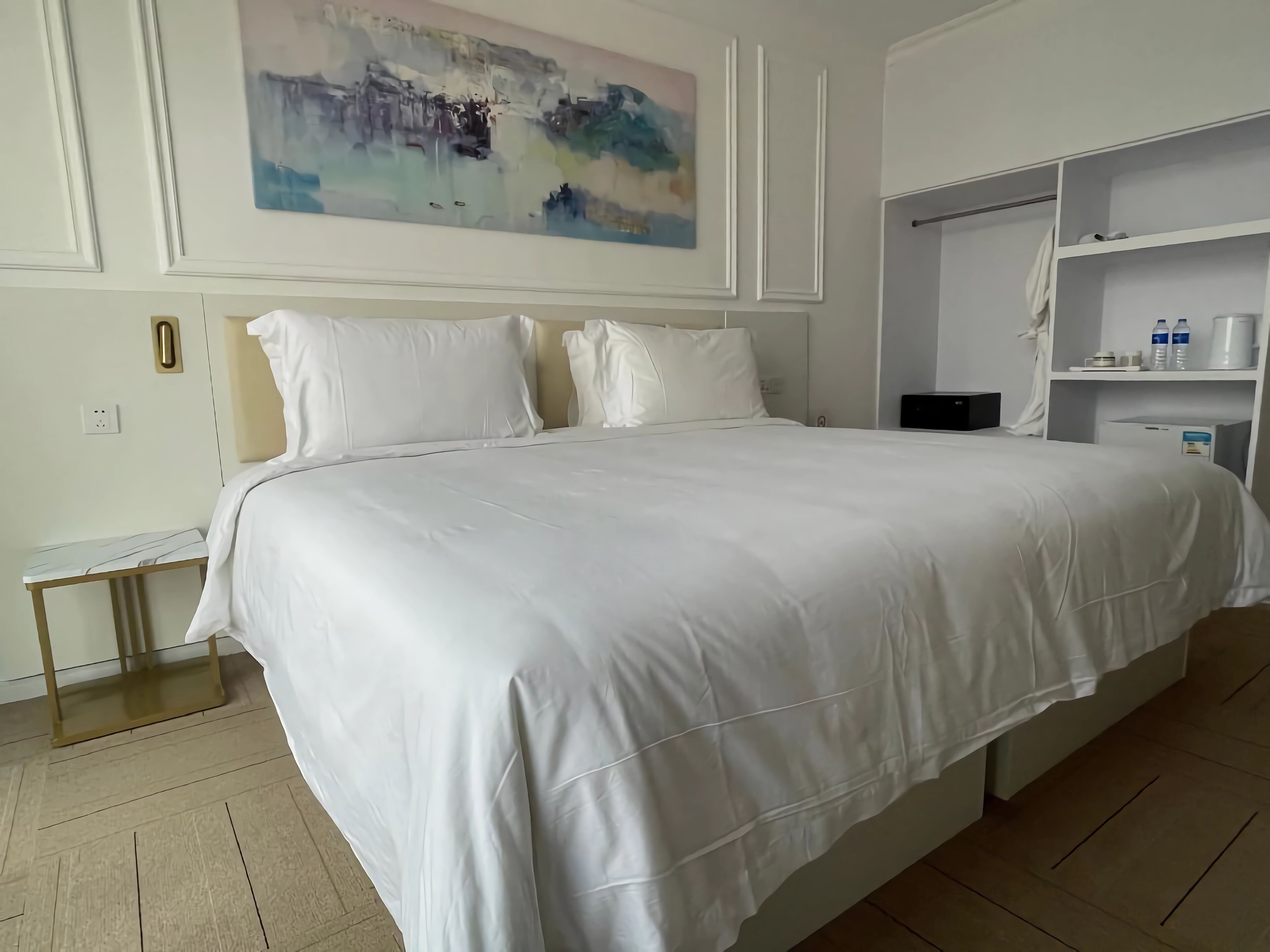 Una cama grande con ropa blanca, una mesita de noche y un cuadro colgado en la pared.