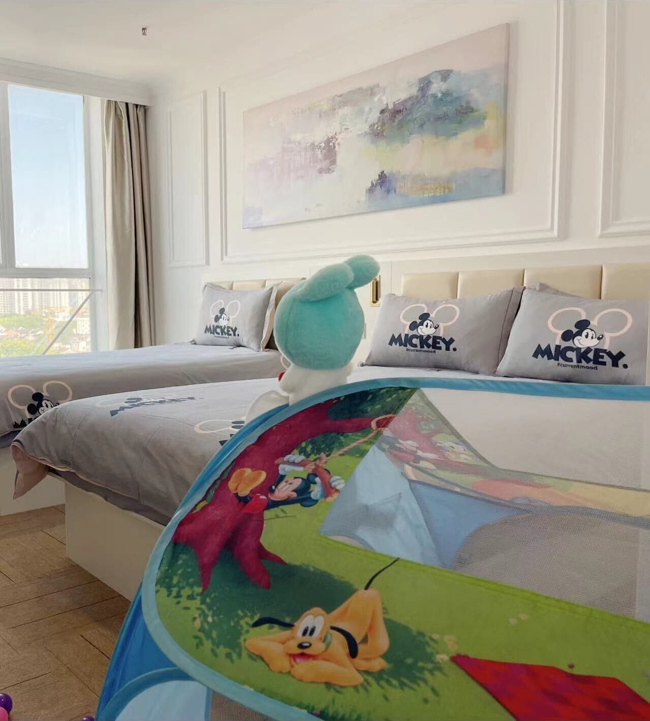 A hotel room with two beds, Mickey Mouse pillows, and a large Mickey Mouse-themed bedspread.