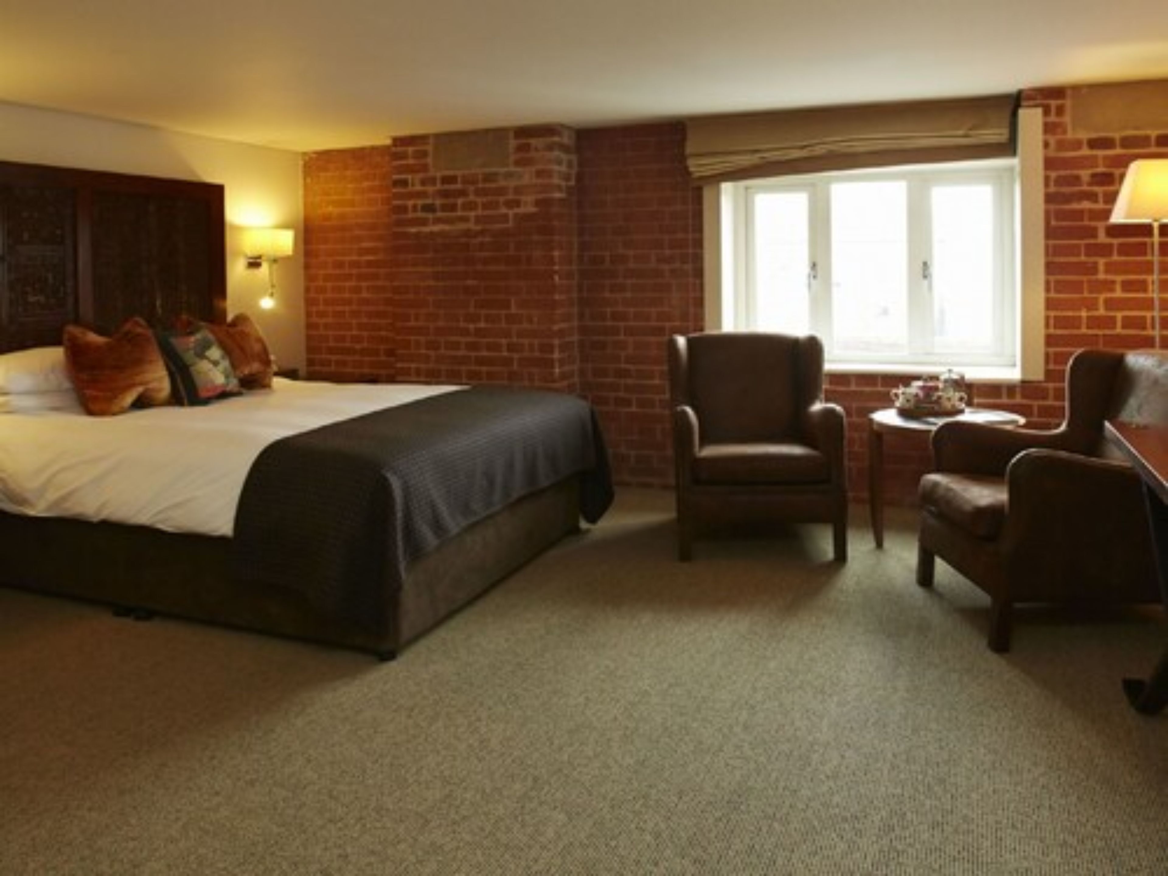 Ein Hotelzimmer mit einem großen Bett, zwei Sesseln, einem kleinen Tisch und einem Fenster mit Blick.