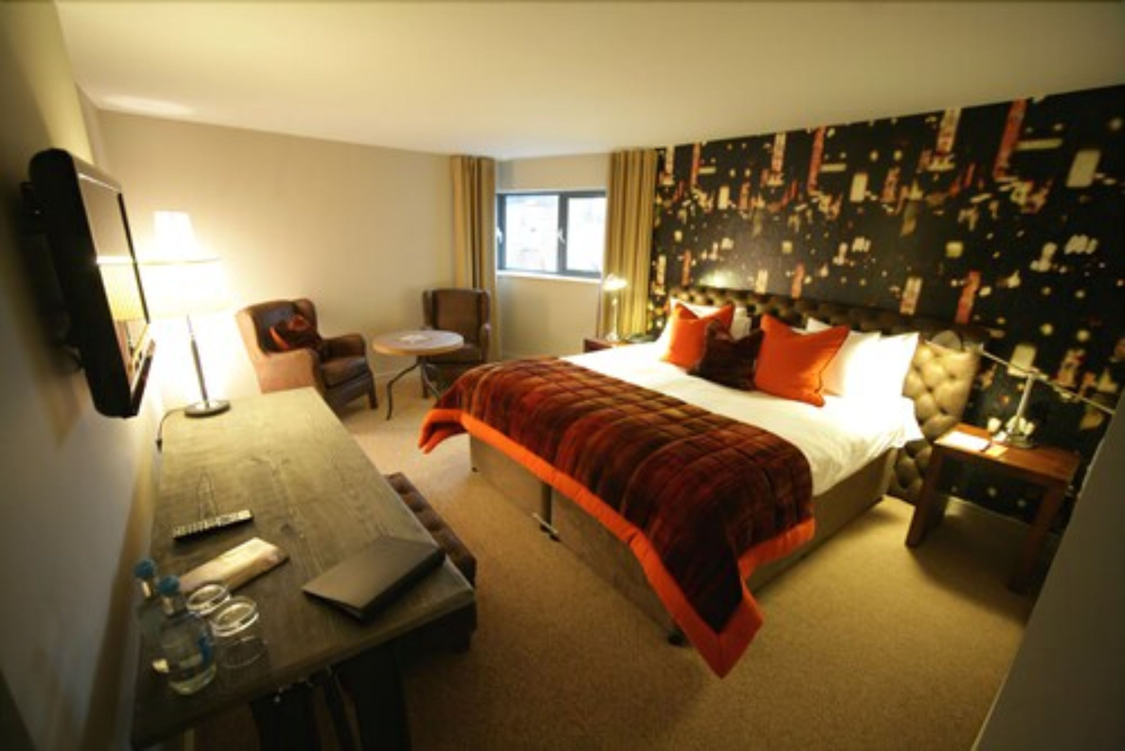 A hotel room with a bed, a desk, a chair, a small table, and a nightstand.