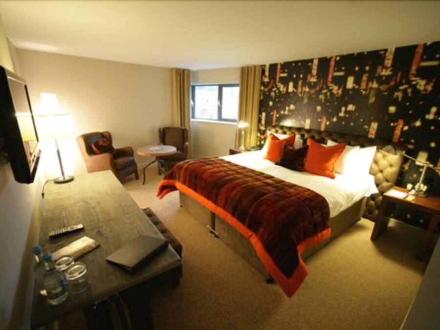 A hotel room with a bed, a desk, a chair, a small table, and a nightstand.