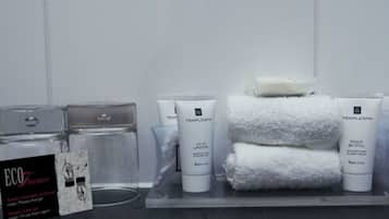 A bathroom with a towel rack holding three white towels, a glass jar, and two white bottles labeled 'TEMPLESPA'.