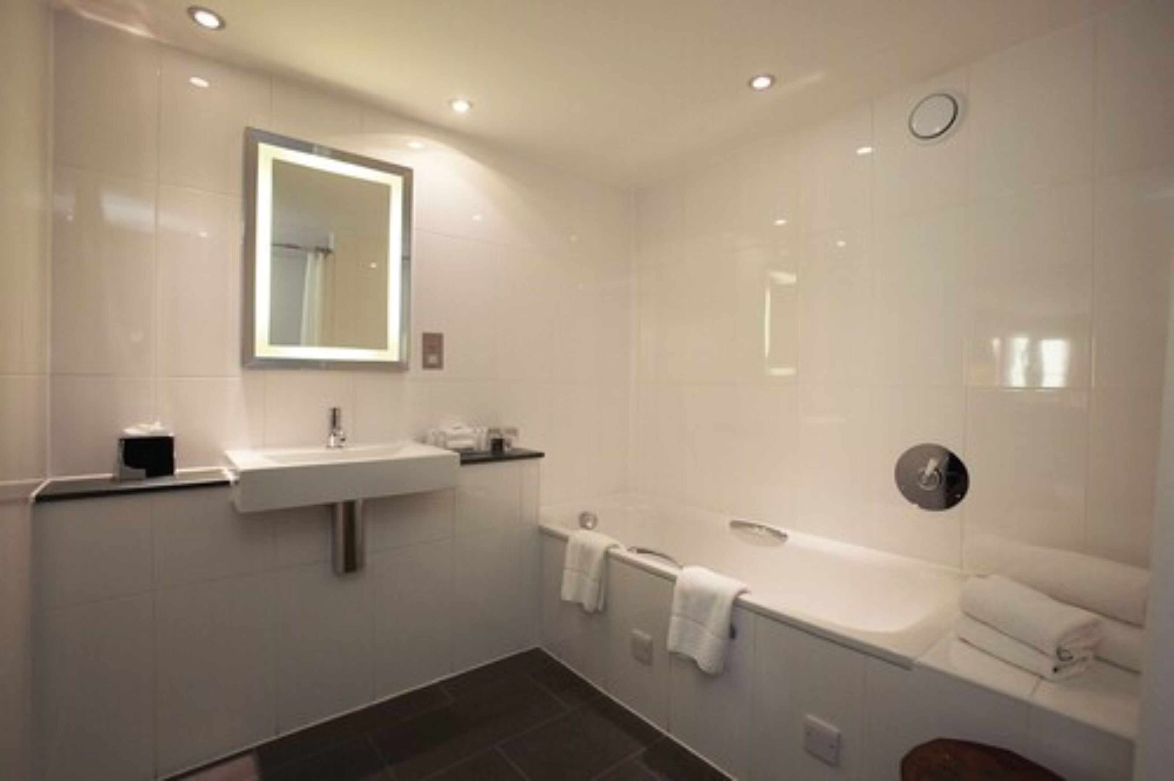 A modern bathroom with a sink, mirror, and bathtub.