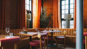 A restaurant with wooden tables and red upholstered booths, brick walls, and large windows with orange curtains. - Salthouse Harbour Hotel and Spa (Ipswich)
