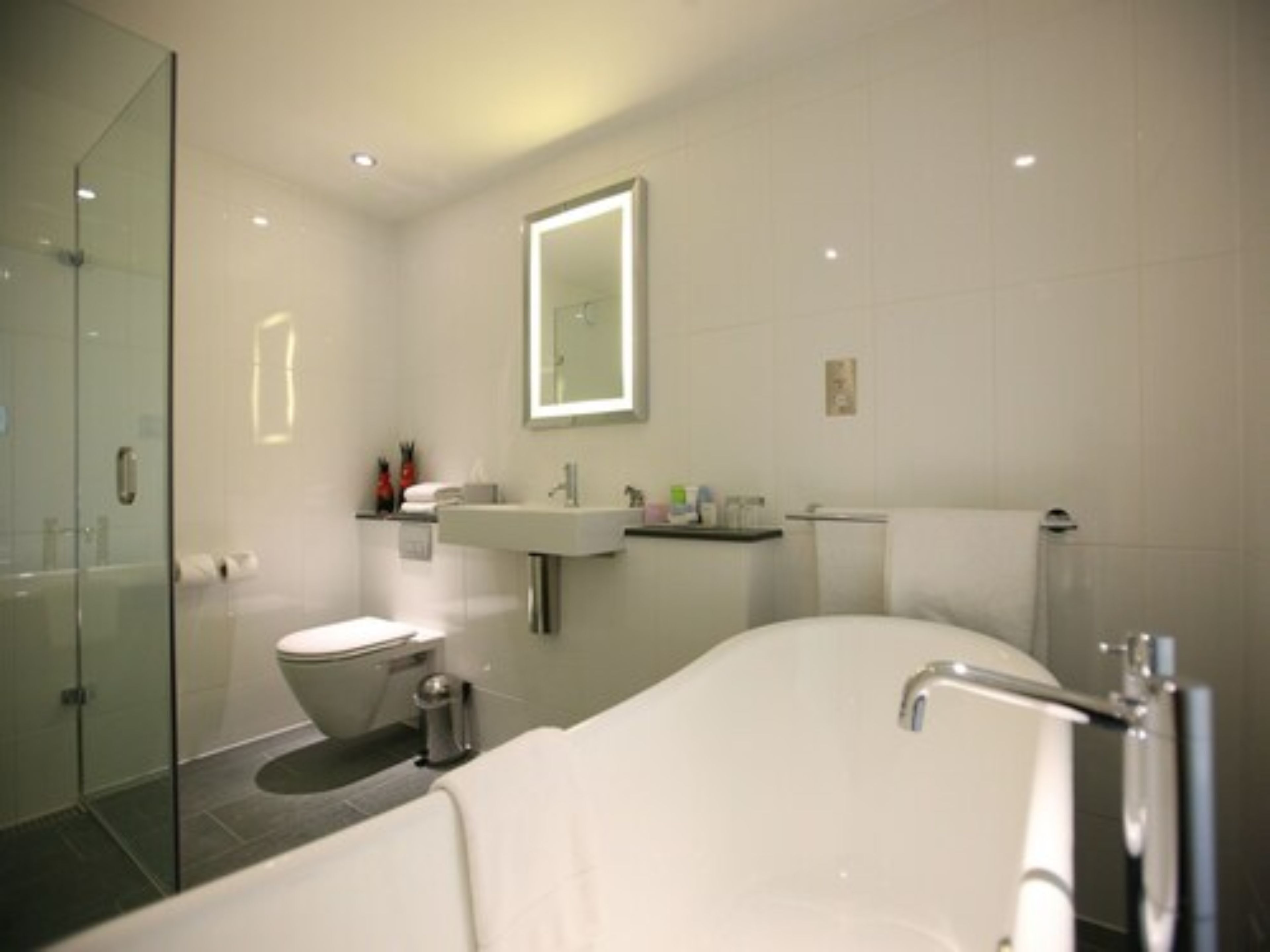 Un baño moderno con cabina de ducha de vidrio, inodoro blanco, lavamanos con artículos de aseo y bañera.