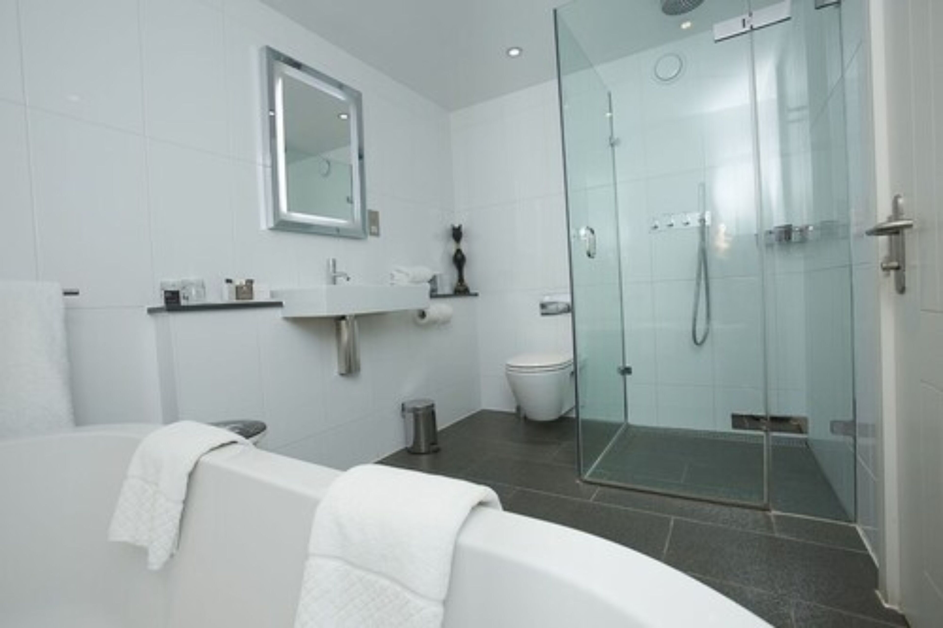 Un baño moderno con ducha de vidrio, bañera y lavabo con espejo.