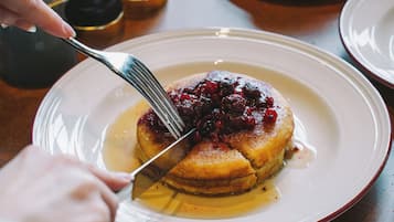 Une assiette de crêpes garnies de fruits rouges et nappées de sirop, une tasse de café, et des salières et poivrières posées sur une table.