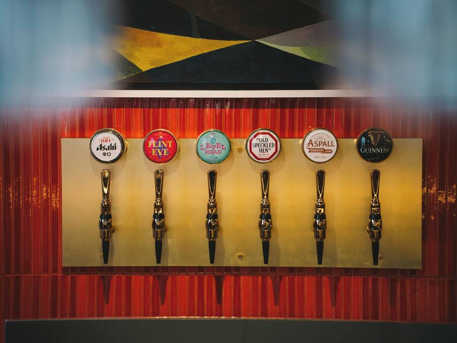 A row of beer taps with labels including 'Asahi,' 'Old Speckled Hen,' 'Guinness,' and others.