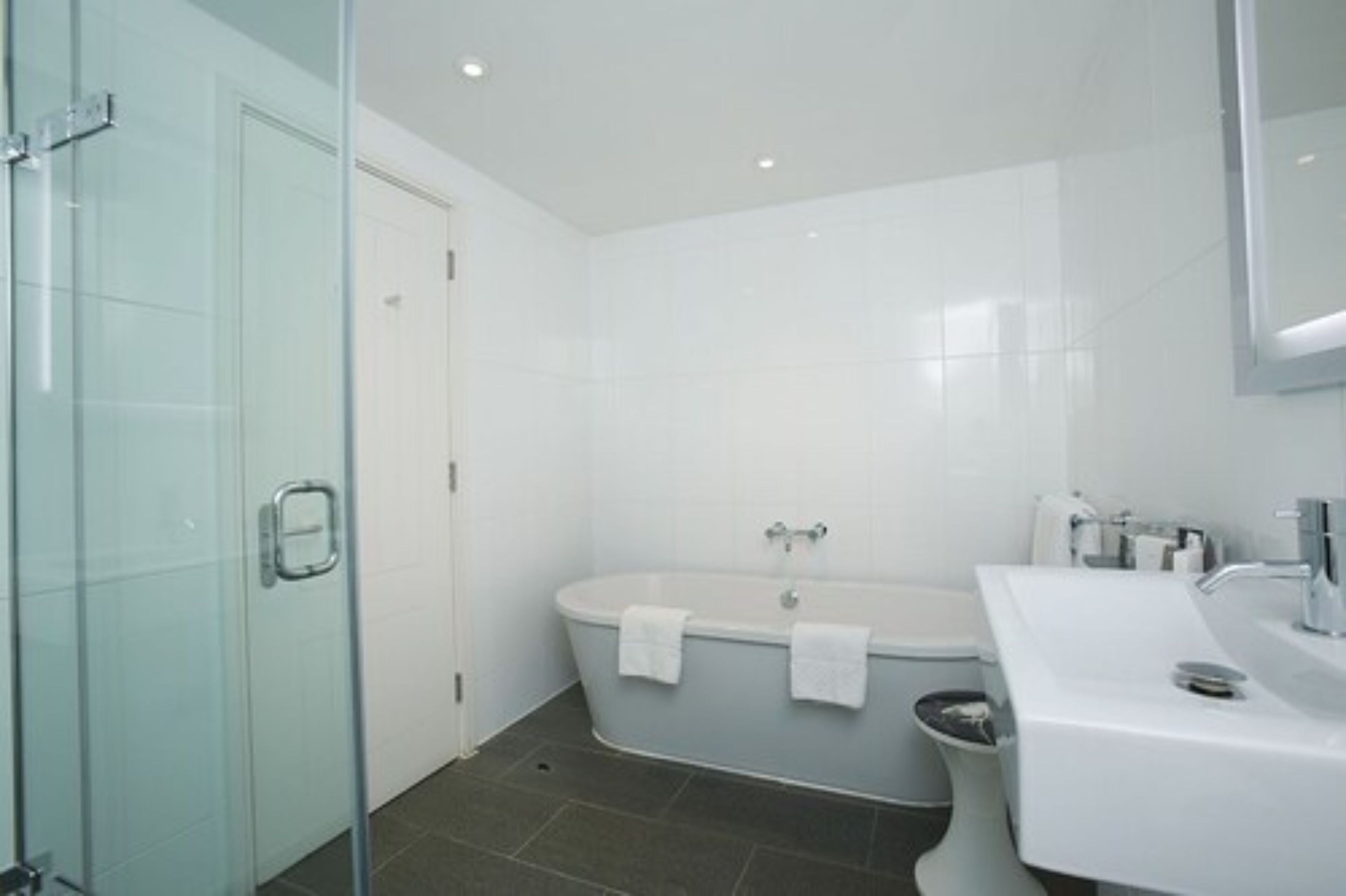 A modern bathroom with a glass shower enclosure, a freestanding bathtub, and a white sink.