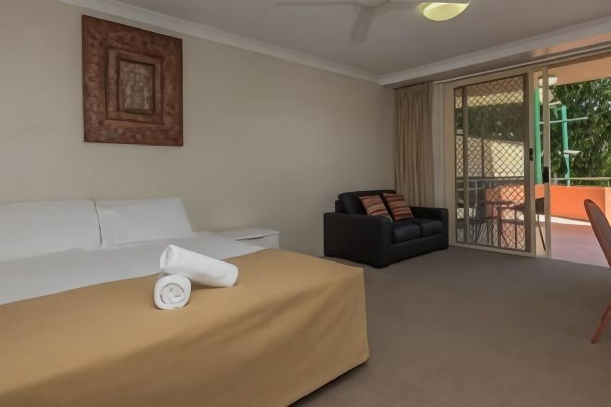 A hotel room with a bed, a sofa, a dining table, and a sliding glass door leading to an outdoor area.