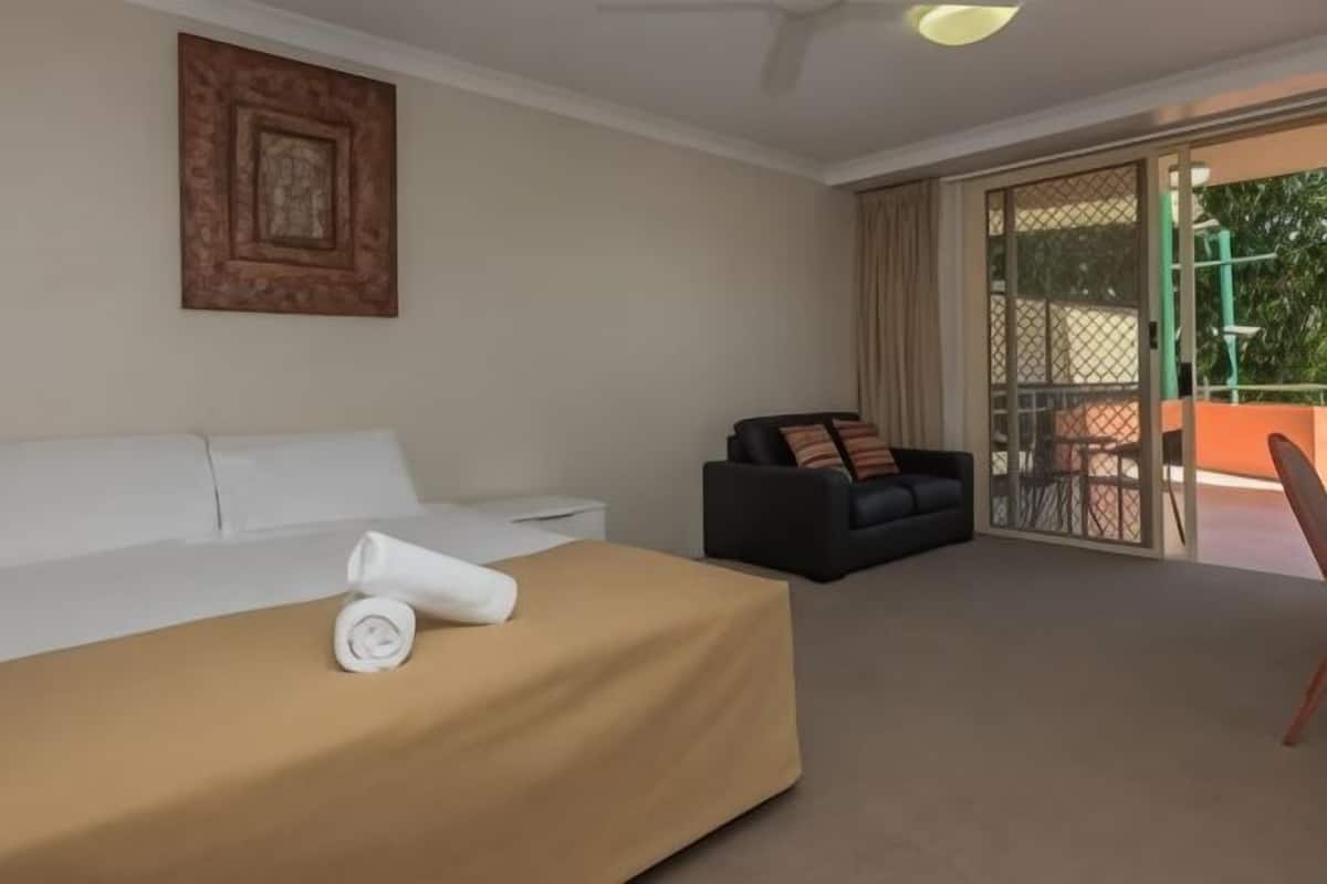 A hotel room with a bed, a sofa, a dining table, and a sliding glass door leading to an outdoor area.