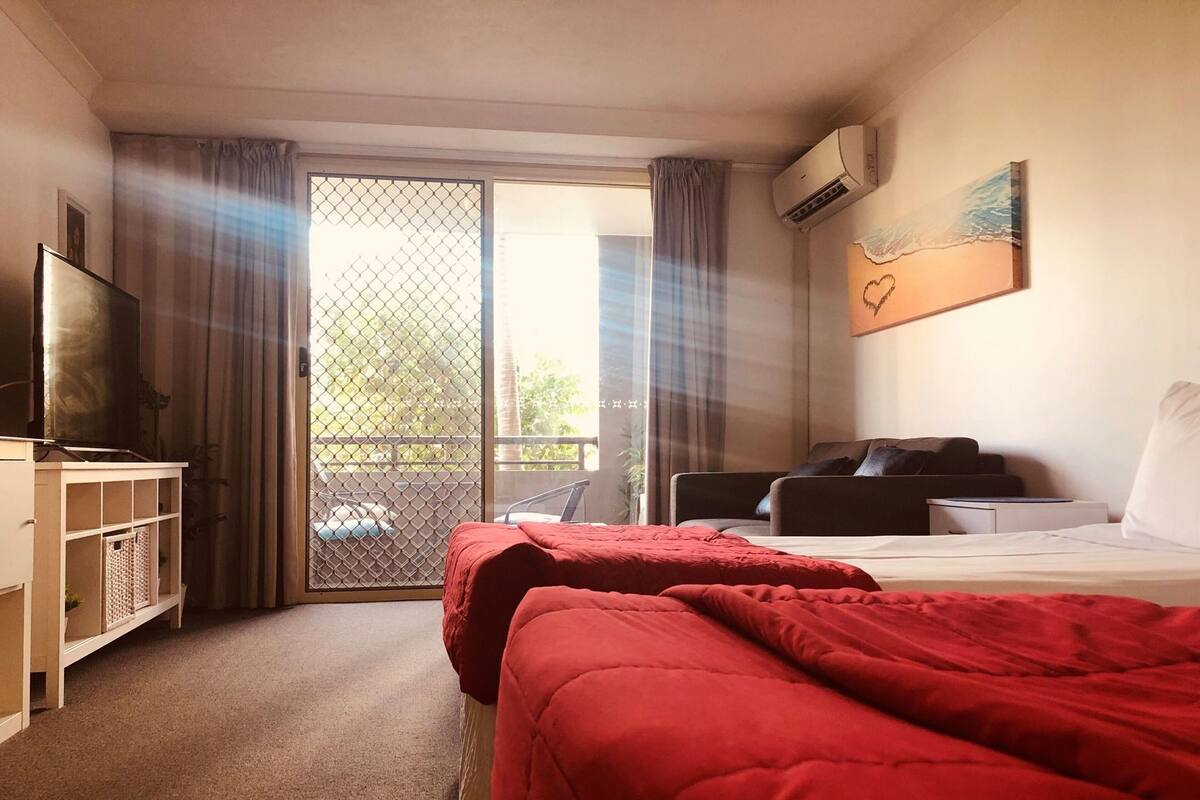 A hotel room with a bed, a TV, a desk, a chair, and a balcony with curtains.