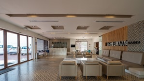 Eine moderne Hotelhalle mit einer Rezeption, einer Sitzecke und Blick auf parkende Autos vor dem Haus.